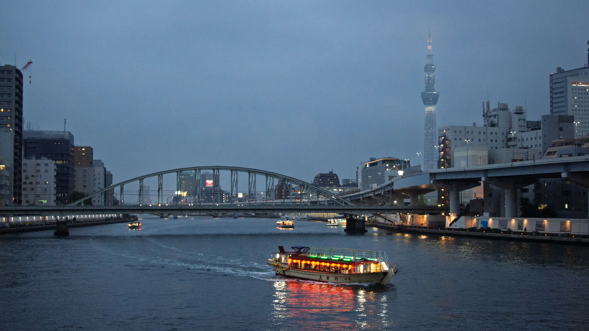 A traditional lantern-lit yakatabune dinner boat on the Sumida River at dusk with the Tokyo Skytree in the background